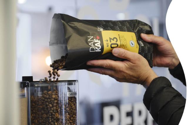 Kaffebønner hældes i bønnebeholder på kaffemaskine