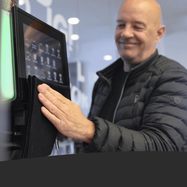 Mand rengør skærm på kaffemaskine
