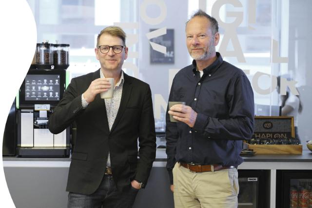 Billede af to mænd, der drikker kaffe foran en kaffemaskine