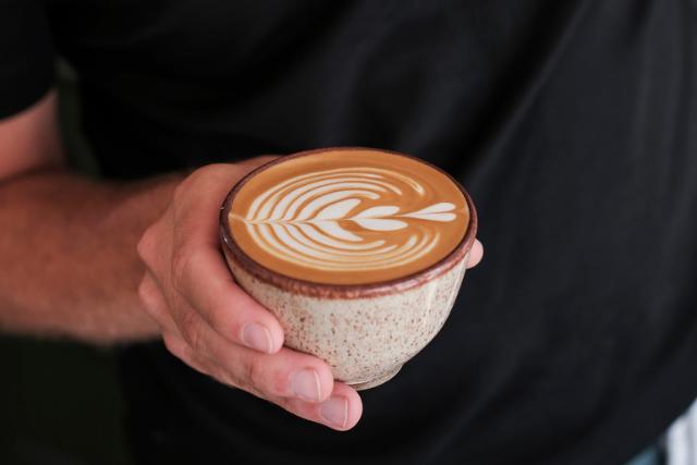 Hånd holder en cappuccino med flot latteart på toppen