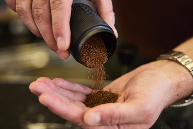 Formalede kaffebønner hældes fra en sort beholder ned i en håndflade