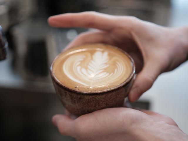 to hænder holder en kop kaffe med flot latteart på toppen lavet i en keramikkop