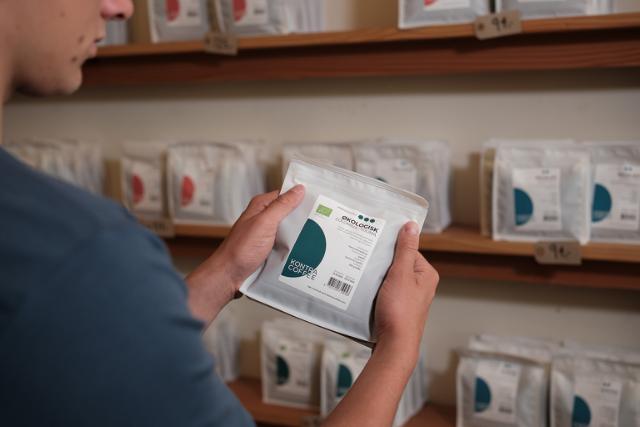 Hænder holder hvid kaffepose med mørkristede kaffebønner fra KONTRA Coffee