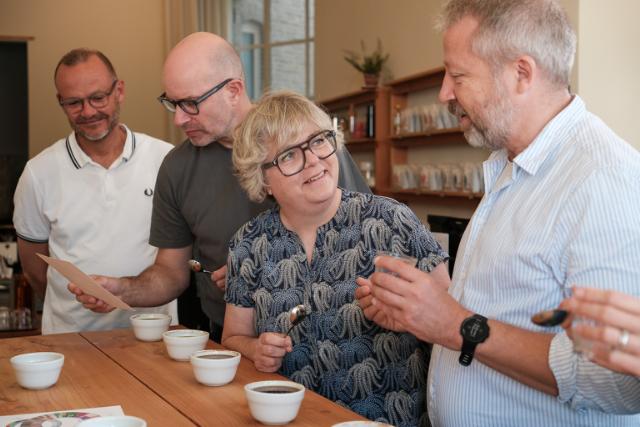 Fire personer staar ved at bord og smager paa kaffe i cupping-kopper