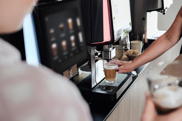kvinde laver kaffe fra fuldautomatisk kaffemaskine