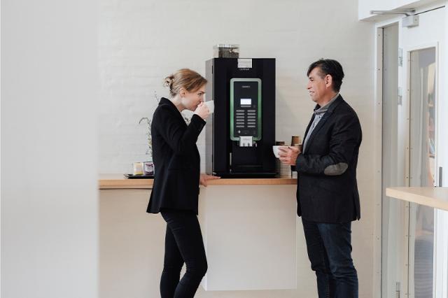 To kolleger drikker kaffe ved leaset eller lejet kaffemaskine