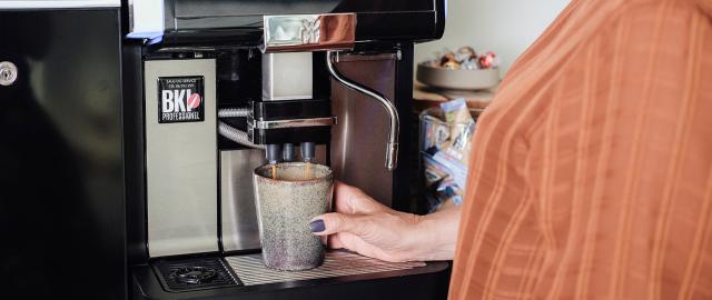 kvinde brygger kaffe på kaffeautomat og prioritere god kvalitetskaffe i virksomheden