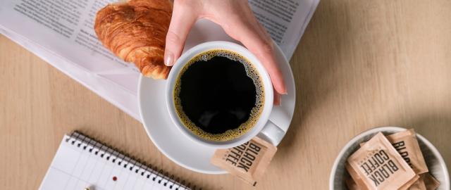 sort kaffe på avis med croissant som gør firmakaffen god på kontoret